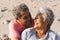 Loving retired multiracial senior couple looking at each other while sitting on sunny beach