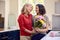 Loving Same Sex Mature Female Couple In Kitchen With Woman Giving Partner Flowers