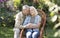 Loving senior spouses resting in countryside, woman sitting in wicker chair and man embracing wife and smiling