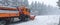 Low-agle of snow ploughing truck cleaning the road after heavy snowfall snowy forest background