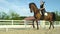 LOW ANGLE: Active girl trotting on her horse around the sandy arena on sunny day