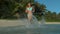 LOW ANGLE: Attractive female tourist runs in the sea and splashes water around