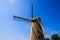 Low angle back view on typical isolated dutch tower stone brick windmill with sails against blue sky