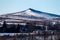 Low-angle of Bennachie snowy sunlit mountain with deciduous trees around clear sky background