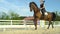 LOW ANGLE: Cheerful English rider trotting around the sandy arena on her horse.