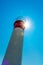Low angle, close-up red and white metal lighthouse, beacon, against blue sky with sun glare from behind causing bokeh, concept, b