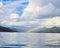 Low-angle of Como lake sunlit forested mountains rainbow cloudy sky background