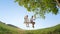 LOW ANGLE: Couple happy kids swinging on a swing under a big tree on a warm day