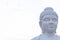 Low angle face shot of a white Buddha statue with bright sky in the background