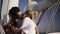 Low angle footage of stylish couple with dreadlocks in white clothes and sunglasses sitting embracing on the bow of the