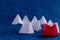 Low angle front close up shot of a red paper boat with many white boats in blue ocean