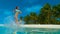 LOW ANGLE: Happy woman jogging in her bikini and splashing glassy ocean water.