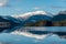 Low-angle of Harstad snowy mountain with a lake reflecting it, sunlit tops against clear sky