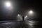 Low angle, looking up at a hooded figure standing in the middle of the road on an atmospheric foggy winters night. UK
