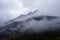 Low-angle of misty, ridged mountains covered with clouds against gloomy sky