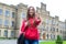 Low angle photo of beautiful pretty showing v-sign to you in camera holding modern schoolbag. Old building is on the background