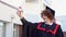 Low angle portrait of happy triumphant male graduate standing near university holding up diploma. From below of young