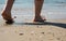 Low angle shot of the bare legs of a person walking through the sandy beach