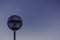 Low angle shot of a blue round sphere on a pole and the moon and the blue sky in the background