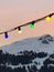 Low angle shot of colorful Christmas lights hanging on a cable on a mountain landscape background