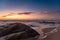 Low angle shot at dusk on beach with sea foam on shore and big boulder