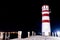 Low angle shot of a lighthouse on a dock by the sea at night