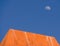 Low angle shot of an orange wall with a visible moon in a blue sky