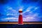 Low angle shot of a red and white lit lighthouse on the road under a blue and purple cloudy sky