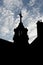 Low angle shot of a silhouette of the part of a church with a cross on top and a cloudy blue sky