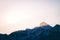 Low angle shot of the sun shining on a peak of a snow covered rocky mountain