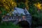 Low-angle stone bridge with a brick mini-house with trees around on it water flowing under at sunset