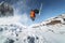 Low angle view athlete skier in an orange jacket does a back flip with flying powder of snow against a clear blue sky