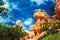 Low angle view beyond green trees on sedimentary sharp tower like red rocks hoodoos against blue sky with clouds