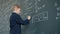 Low angle view of clever schoolboy writing formulas with chalk on blackboard