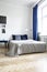 Low angle view of a cozy double bed in a corner of a bright bedroom interior with navy blue textiles and parquet floor