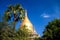 Low angle view on golden isolated dome of pagoda against blue sky framed by trees and palm tree -  Bagan, Myanmar