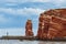 Low angle view of the Helgoland rock pillar Lange Anna showing the red rock cliffs against a cloudy and blue sky