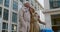 Low angle view of positive senior couple with suitcase standing outside hotel building