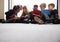 Low angle view of primary school friends sitting together in front of a window in a school corridor looking at tablet computers to