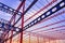 Low angle view of red and blue metal castellated beam structure of large industrial building in construction site at sunset