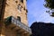 Low angle view on stone facade of typical French house and balcony with ancient ornate lattice work. Church on mountain top