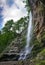 Low angle view of a waterfall surrounded by rocks and greenery under a cloudy sky in Devil`s Pass