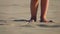 The low-angled shooting of legs of little girl walking in the sand on the beach