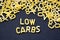 Low carbs phrase spelled with raw letter-shaped pasta on blackboard background