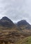 Low cloud on the tops of the Three Sisters Mountains in Glen Coe, with waterfalls running down between the peaks, and some snow.