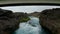 Low flight above water flowing in wild creek between rough rocky banks. Fly under steel road bridge. Iceland