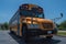Low front right angle view of yellow American public school bus showing door with sun directly overhead casting a shadow down on