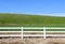 Low grassland hillside hills pasture with bright sunny blue sky and wooden white picket farm livestock fence