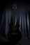 Low key image of the silhouette of an acoustic guitar on a stage with a lightly illuminated black backdrop curtain in the