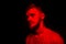 Low key portrait of bearded young man in red light on black backdrop